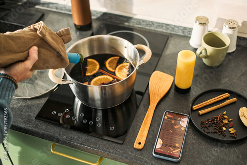 Cuadro en lienzo Adult hand pouring wine from bottle into saucepan with orange slices on inductio