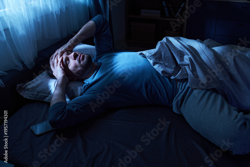 Fotografie Adult man lying in bed holding head with both hands appearing distressed, smartp