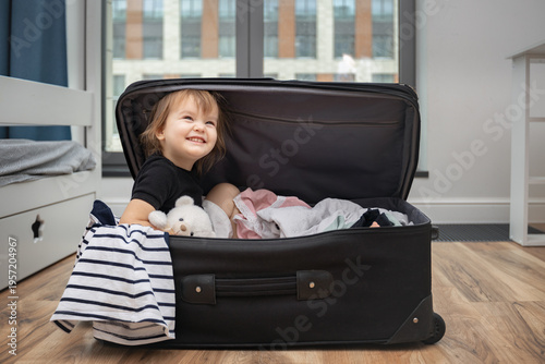 A baby girl sits in an open suitcase as the family gets ready for vacation.