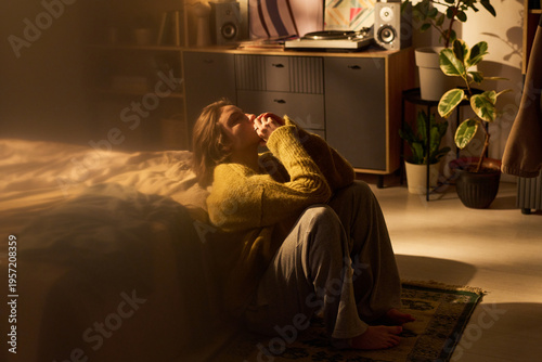 Photos Young woman sitting on floor beside bed holding hands near face appearing though