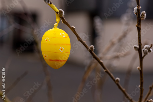 Colorful yellow Easter egg hanging on tree branch in early spring sunlight, capturing the essence of celebration and renewal outdoors