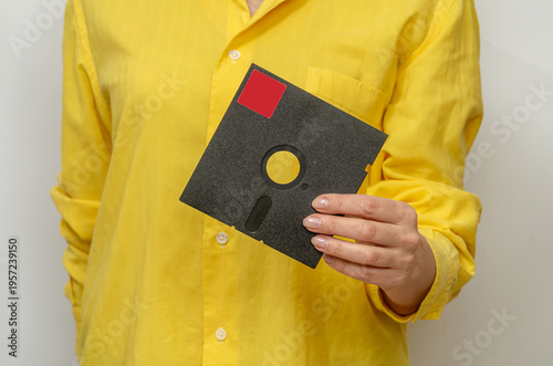 Old black floppy disk in female hands. Vintage computer data storage device used in early computers.