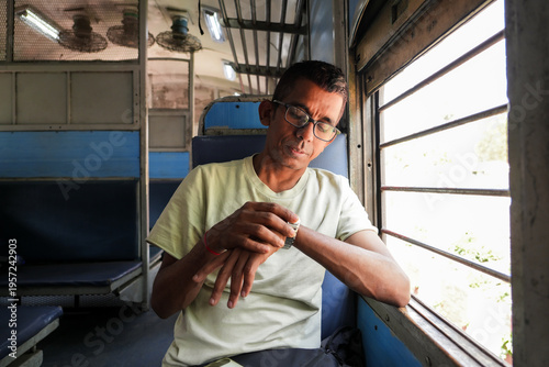 An Indian man sitting by the train window checking the departure time. Daily commute to work concept. 