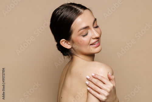 Skin care model. Beautiful young woman with perfect skin touching her face and posing against beige background.