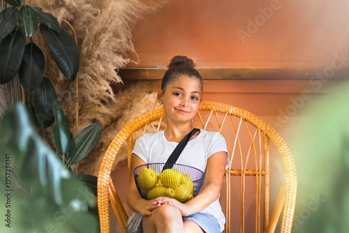 A beautiful teenage girl is sitting on a wicker chair on the porch with a basket full of lemons.
