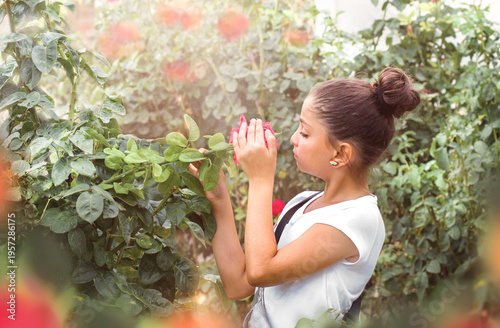 A beautiful teenage girl holds and smells a red rose in a decorative garden