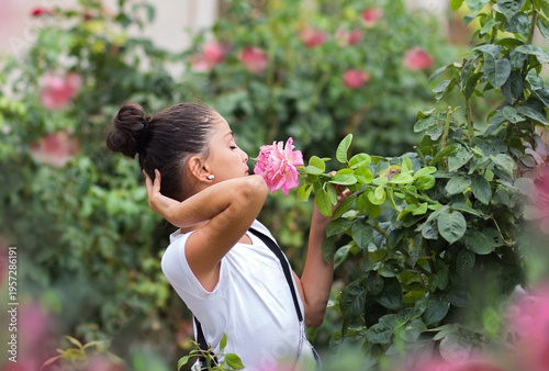 A beautiful black-haired teenage girl smells a blossoming rose in the garden.