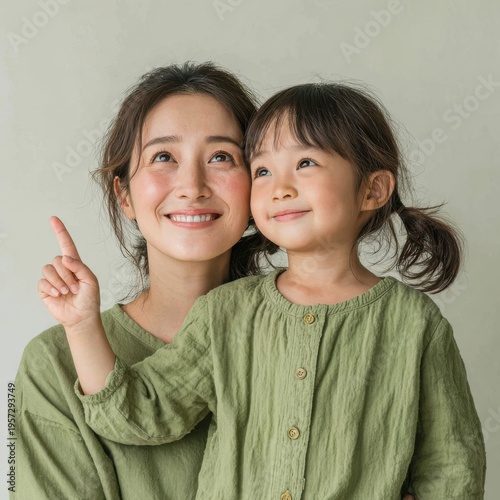 Close-up of a smiling mother and daughter looking upwards and pointing with a soft neutral background