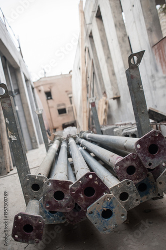 Sturdy steel props are neatly stacked on the ground at a construction site. Surrounding frames rise high, showcasing the busy progress of building in an urban setting