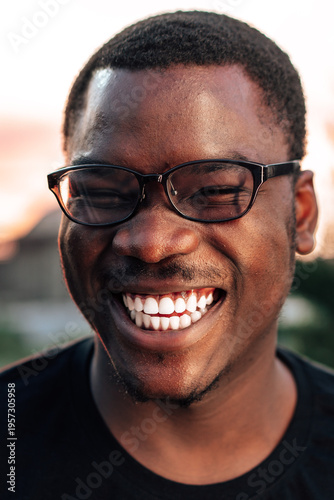 Man smiles widely while wearing glasses during sunset in outdoor setting