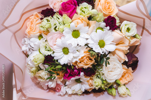 Mixed bouquet of various types of flowers and colors. Delicate pastel, red and pink roses, white chrysanthemums decorated with green leaves. Floristry and floral design concept.
