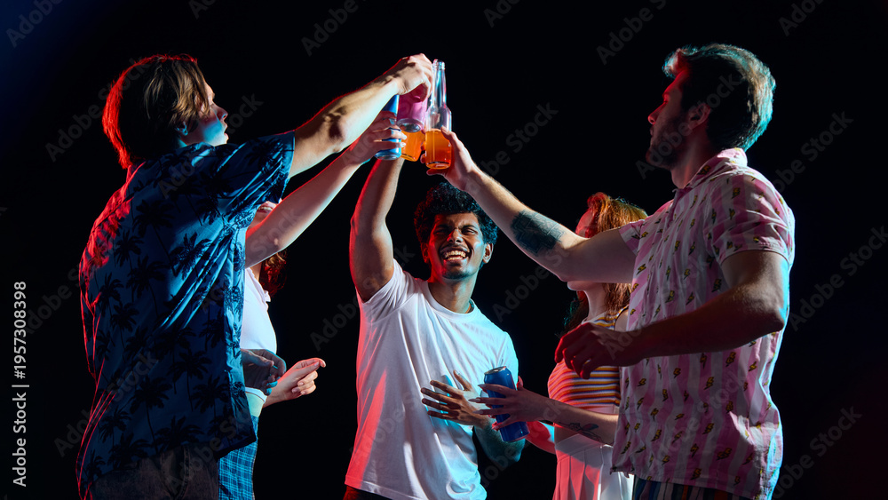 Naklejka premium Friends clinking bottles and cans celebrating party moment in dark studio. Concept of celebration campaigns, beverage advertising, friendship moments and lifestyle branding.