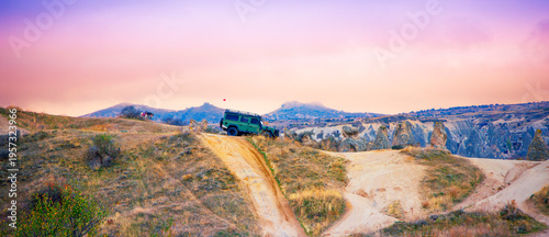 Foto Off-road green SUV, 4x4 driving on a dirt ridge in a vast desert canyon landscape at sunset