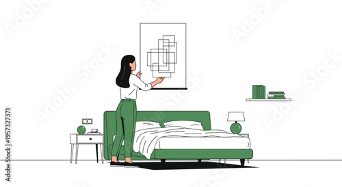 A woman is hanging an abstract picture frame above a green bed in a simply furnished bedroom.