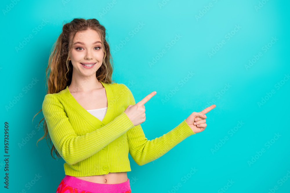Naklejka premium Cheerful young woman pointing energetically against a bright turquoise background in casual attire conveying happiness and positivity