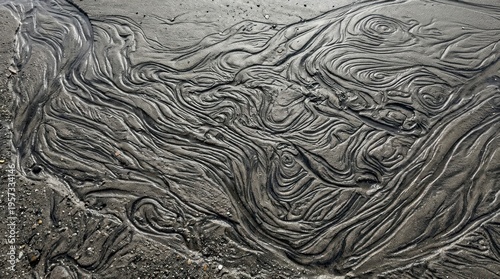 Water flows across a dark, sandy beach, creating intricate, swirling patterns and ripples in the wet sediment.