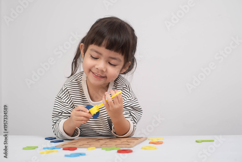 Cute preschool girl playing with colorful educational toy, improving fine motor skills and early math learning. Happy child focusing on number puzzle activity at home or kindergarten classroom.