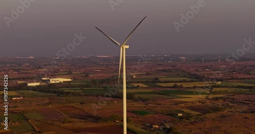 Golden hour aerial view of wind turbines across rural farmland, with rotating blades under a warm orange sky, showcasing clean energy and a serene countryside landscape of Gujrat, India