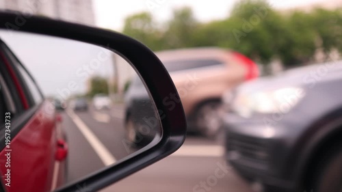 View in the rear view side mirror of a automobile, driving a red car along the road