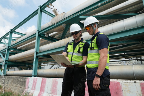 A team of male staff, including male inspectors and foremen in uniforms and helmets, along with engineers reviewing blueprints and planning, were inspecting maintenance work at an oil and petrochemica