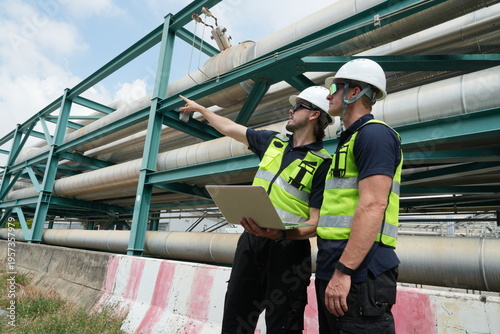 A team of male staff, including male inspectors and foremen in uniforms and helmets, along with engineers reviewing blueprints and planning, were inspecting maintenance work at an oil and petrochemica
