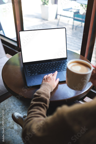 Vertical mockup image of a woman working on laptop computer with blank white desktop screen while drinking coffee in cafe