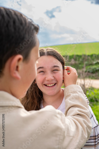 Boy placing daisy behind smiling girl’s ear outdoors