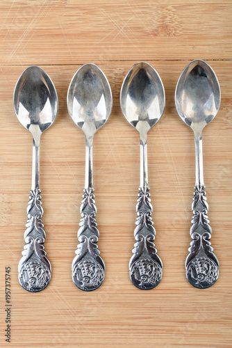 A top view of four vintage metal teaspoons arranged vertically on a wooden surface.
