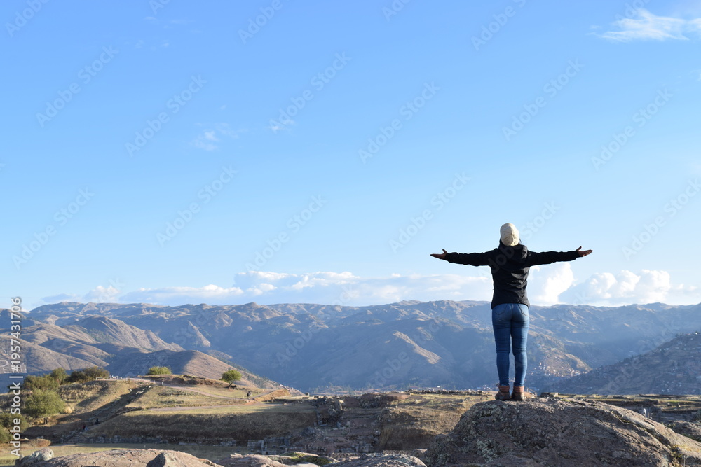 Obraz premium Successful traveler returns with open arms to the pictures Rear view image of a female traveler Saqsaywaman Inca archaeological site. Cusco Peru