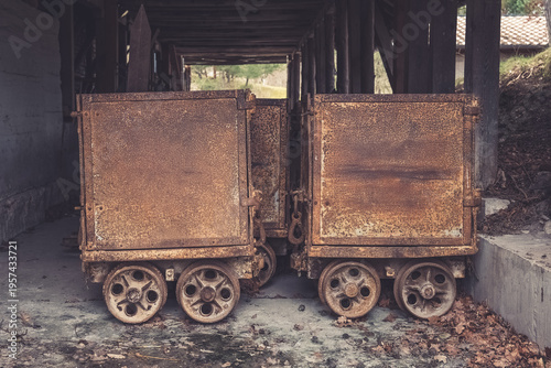Old mining carts rest quietly under weathered wooden beams in an abandoned site, hinting at forgotten labor and history