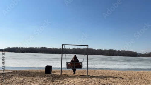 Woman sitting on swing bench by frozen lake, slow living and mindfulness concept, back view, peaceful nature pause, connection with nature and mental balance outdoors.