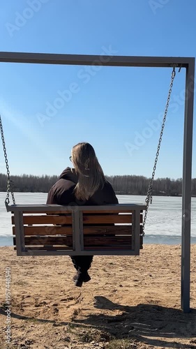 Woman sitting on swing bench by frozen lake, slow living and mindfulness concept, back view, peaceful nature pause, connection with nature and mental balance outdoors.
