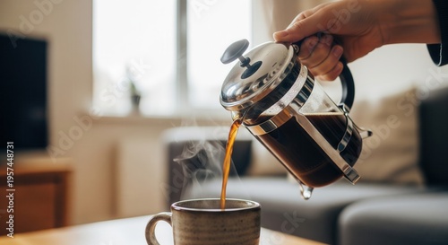 A hand pours freshly brewed coffee from a French press into a mug.