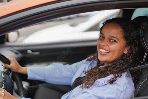 Happy african girl smiling on camera while sitting inside a car - Driving licence, insurance and young people lifestyle concept