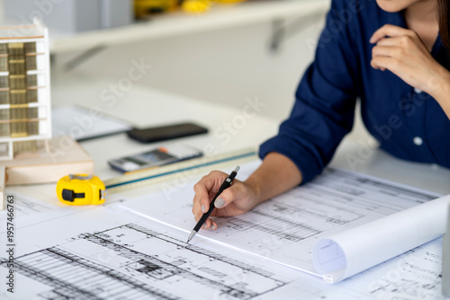 Cuadro en lienzo Female Architect Working on Blueprint Drawing with Pencil at Desk with Building