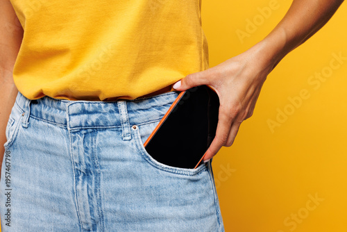 Close up cropped photo shot young woman int-shirt casual clothes hold put into pocket mobile cell phone with blank screen workspace area isolated on plain yellow orange background Lifestyle concept