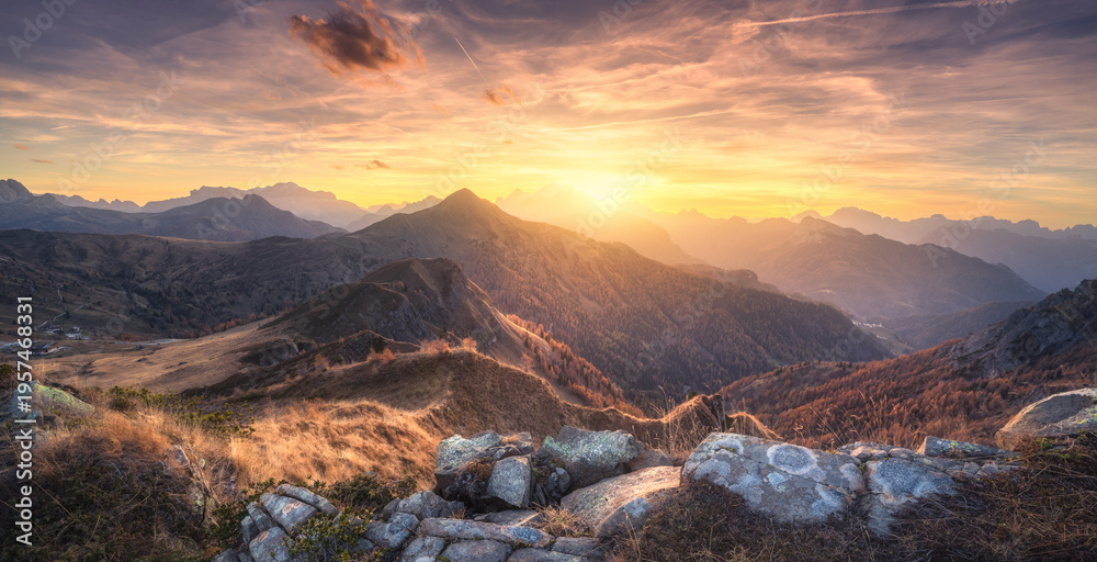 Fototapeta premium Stones and mountains at colorful sunset in autumn in Dolomites, Italy. Colorful landscape with rocks, mountain ridges, hills, orange grass and forest, golden sky with clouds in fall. Hiking. Nature