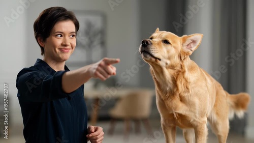 Caucasian woman in dark shirt points finger seriously at golden retriever dog, showcasing a moment of interaction in a modern living room setting
