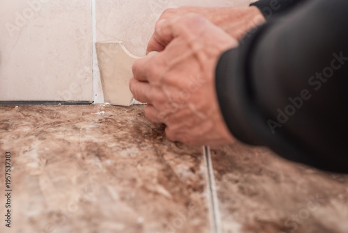 Male worker smoothing silicone sealant between floor and wall using plastic spatula. Hand using scraper to smooth silicone sealant on bathroom wall corner