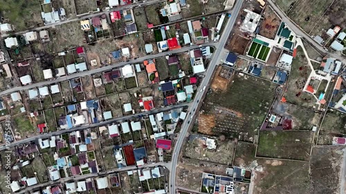 Aerial view of suburban neighborhood with colorful houses. Roads divide residential plots with green spaces. No people visible in frame