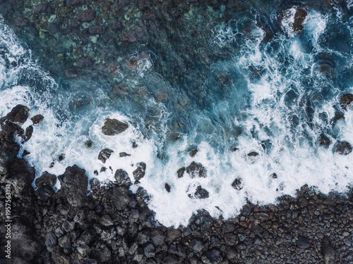 Foto Aerial top-down view of turquoise ocean waves crashing against a rugged rocky shoreline