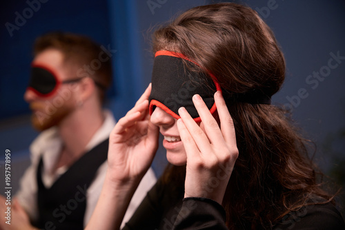 Young woman playfully adjusting blindfold on male companion indoors