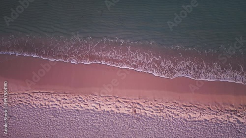Loopable top down view of a beach foreshore at sunset in slow motion with gentle waves moving over wet sand and golden reflections