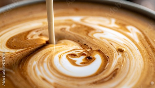 A close-up shot of a creamy liquid being poured into a cup of coffee creating an artistic swirl pattern. The mixture has a rich brown color with white milk blended in. 