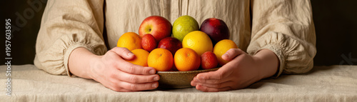 Person holding rustic bowl filled with fresh colorful fruits including apples, oranges, lemons, and plums on linen covered table, evoking natural and cozy feeling