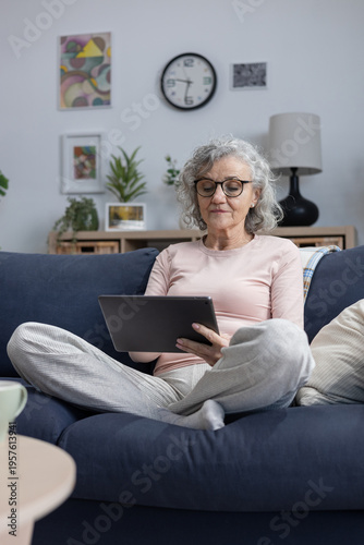 Senior woman relaxing on sofa using digital tablet