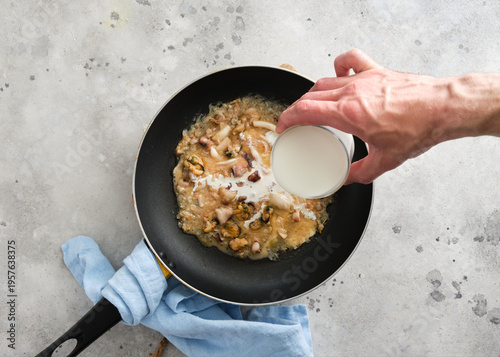 Cooking a dish with seafood and cream in a frying pan on a kitchen counter during the day