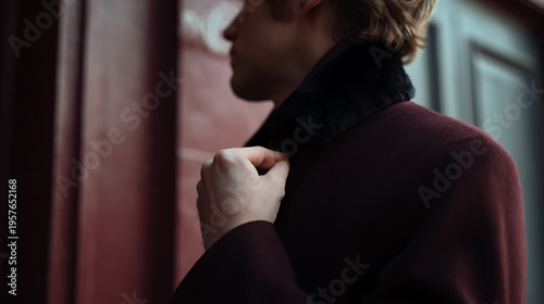 Stylish man adjust coat collar against a warm toned background, partial view, showing elegant fashion and a contemplative mood outdoors