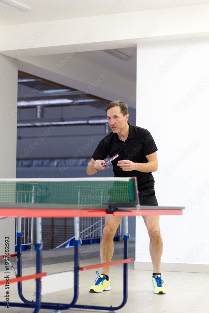 Fototapeta premium Ready stance of a male table tennis player in black shirt in gym.