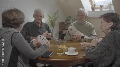 Senior man holding dog in lap and playing cards with friends